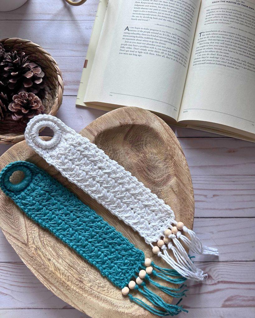 two crochet bookmarks laid in a heart shape wood bowl beside an open book.