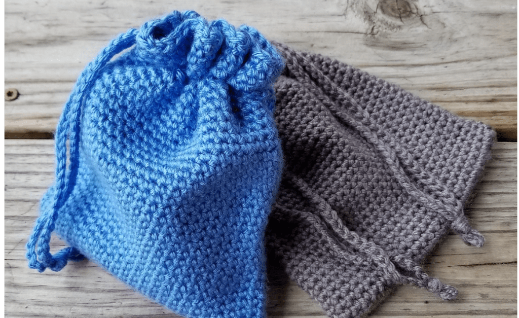 a drawstring crochet pouch in blue and gray, laid out on a table for dice or other game items.