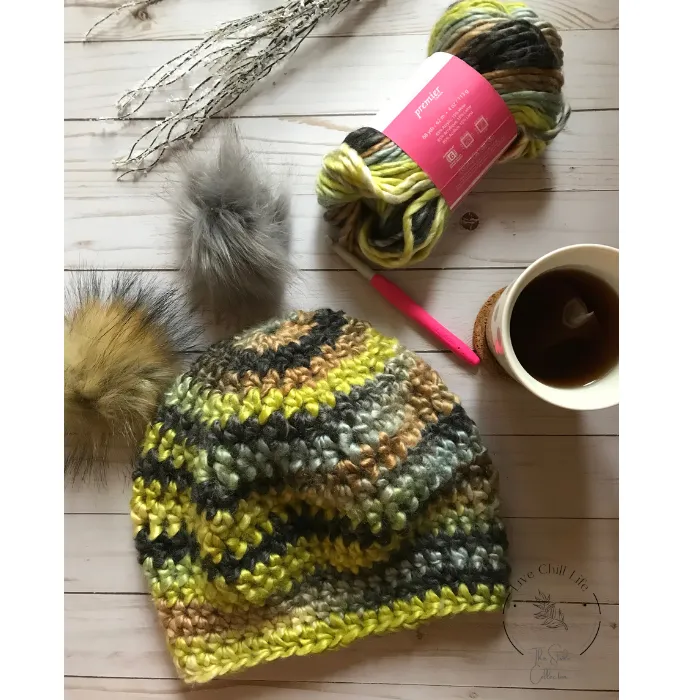 Crochet hat with yarn, cup of tea and faux fur pom pom