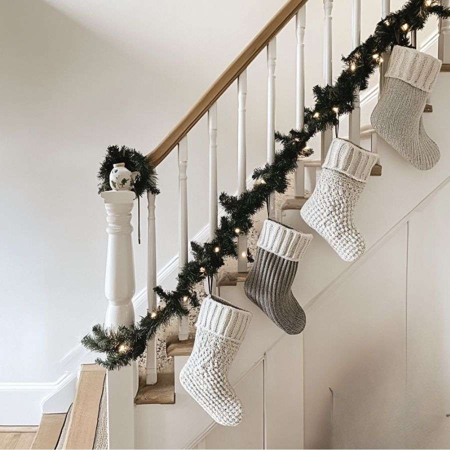 a bannister draped with pine garland, fairy lights and knit christmas stockings