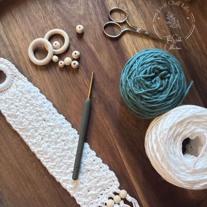 crochet bookmark with balls of white and teal green yarn, crochet hook and wood beads