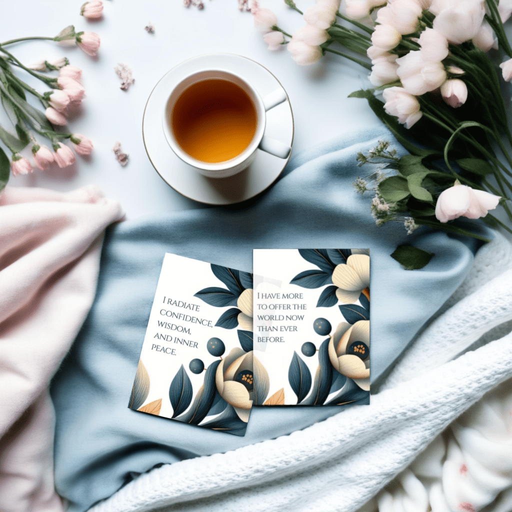affirmation cards for women over 50 laid out on a table with a cup of tea and fresh pink flower bouquets