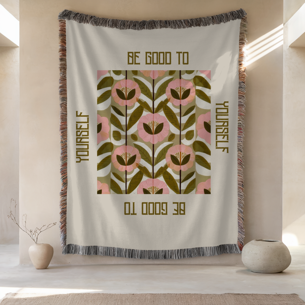 self care fringe blanket hanging on a wall that reads "be good to yourself" with neutral calming color palette