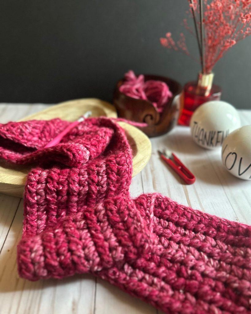 chunky yarn blanket textured stitches up close made with pink gradient yarn, flowers on the table and yarn is in a wood y arn bowl