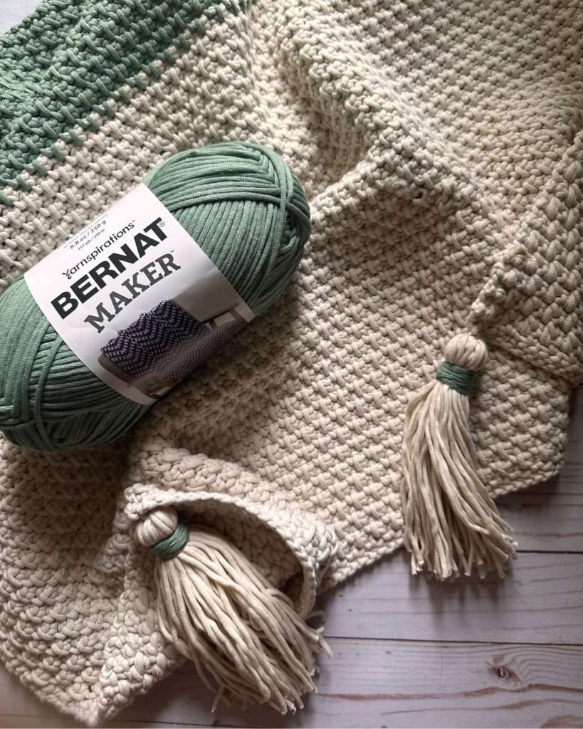 a sage green and cream crochet blanket with tassels